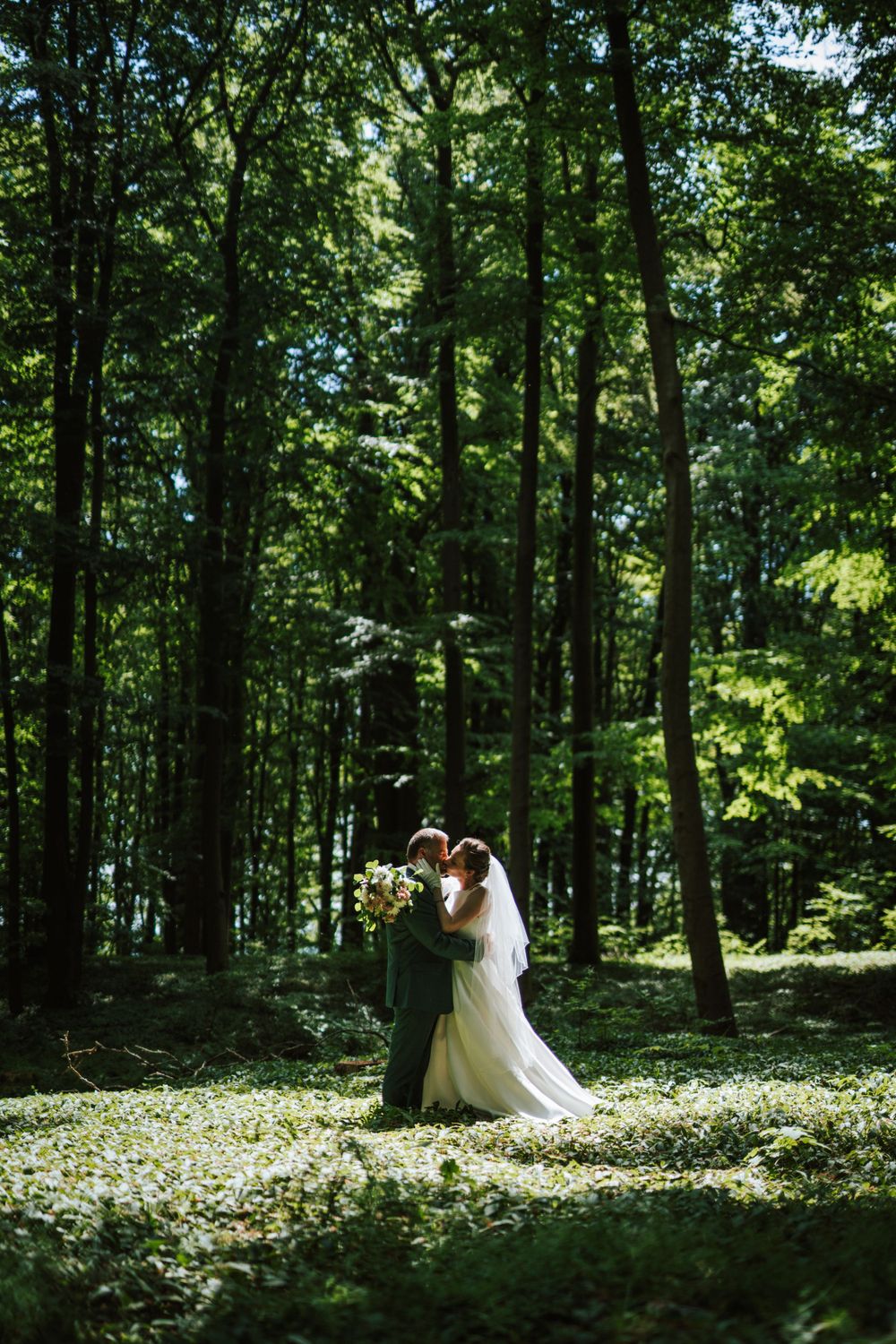 Wedding couple shares intimate moments in a serene woodland setting with scattered wildflowers.
