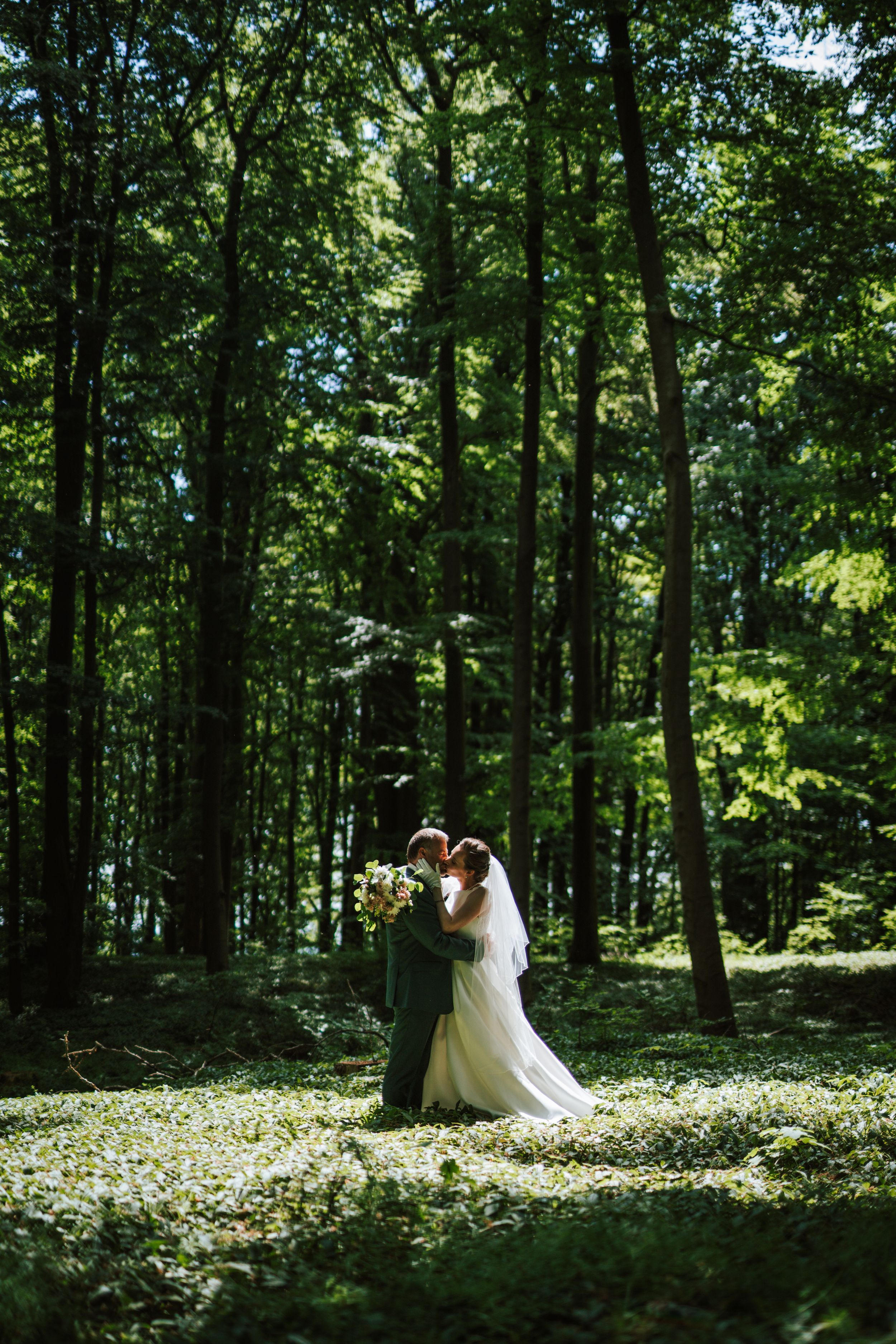 Wedding couple shares intimate moments in a serene woodland setting with scattered wildflowers.