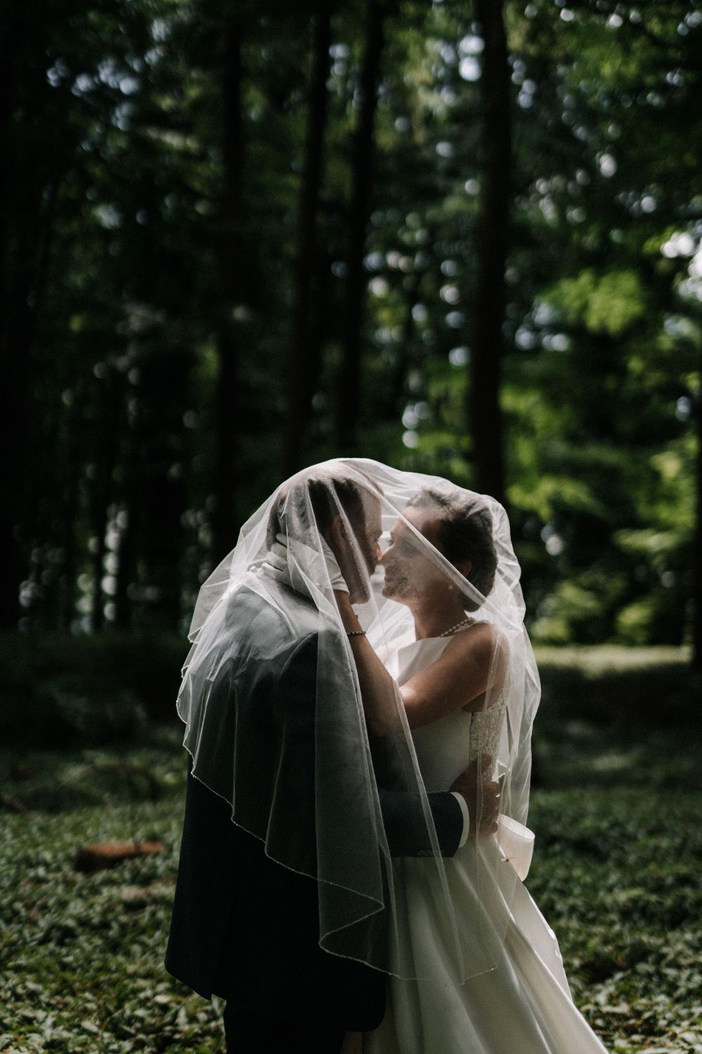 Ethereal wedding scene with flowing veil captures in a forest setting.
