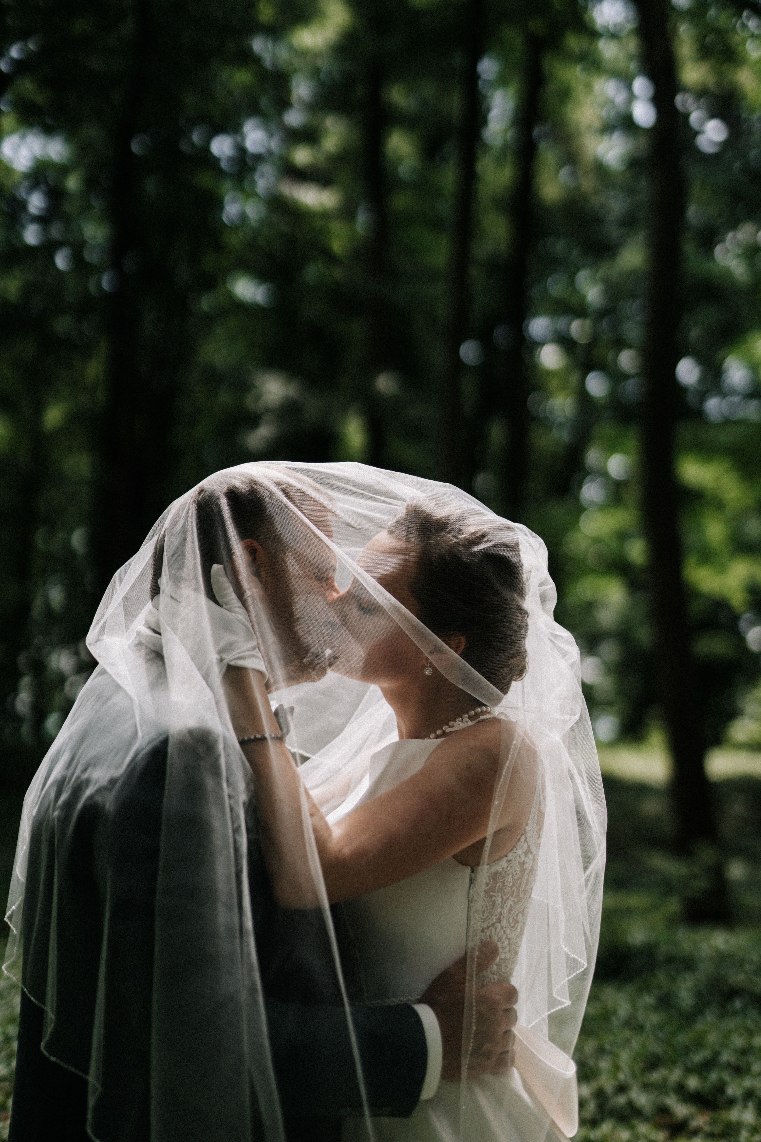 Artistic black and white portrait of newlyweds sharing a tender moment under a flowing veil.