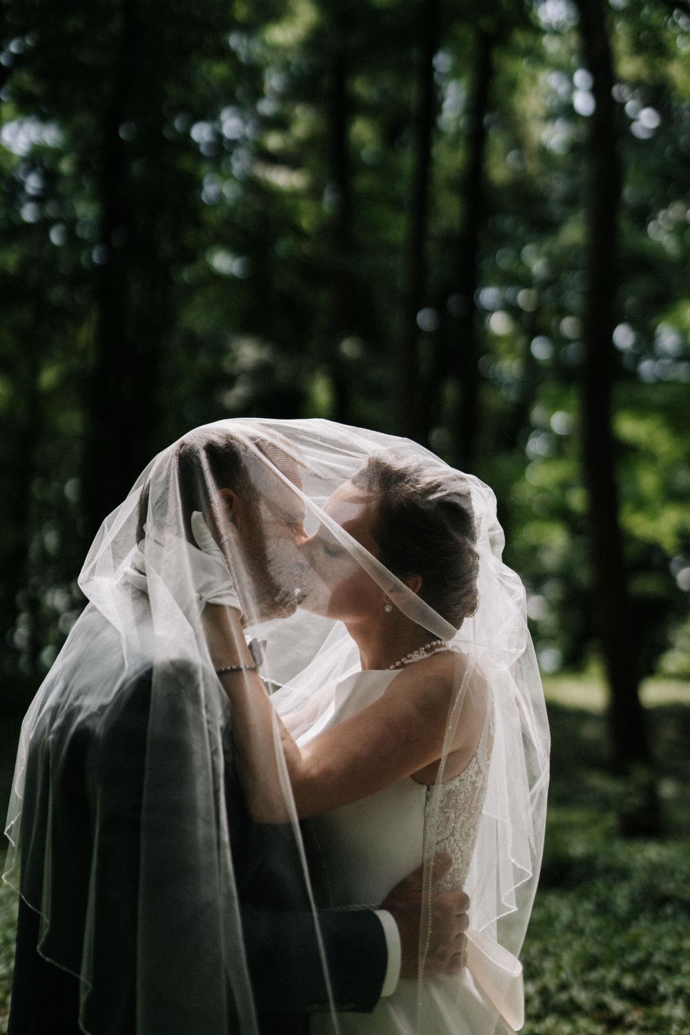 Artistic black and white portrait of newlyweds sharing a tender moment under a flowing veil.