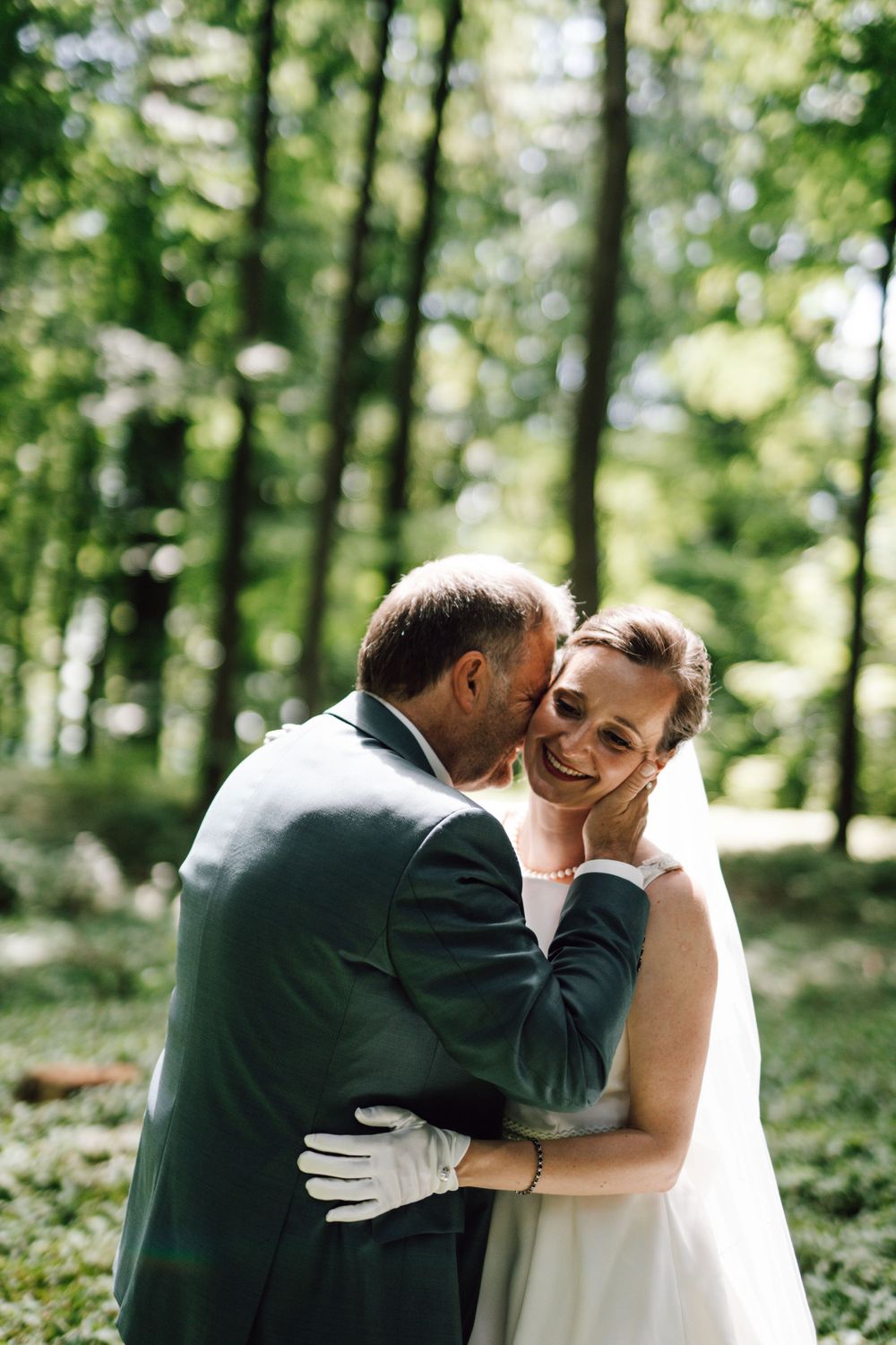Romantic wedding couple shares an intimate moment in a sun-dappled forest.