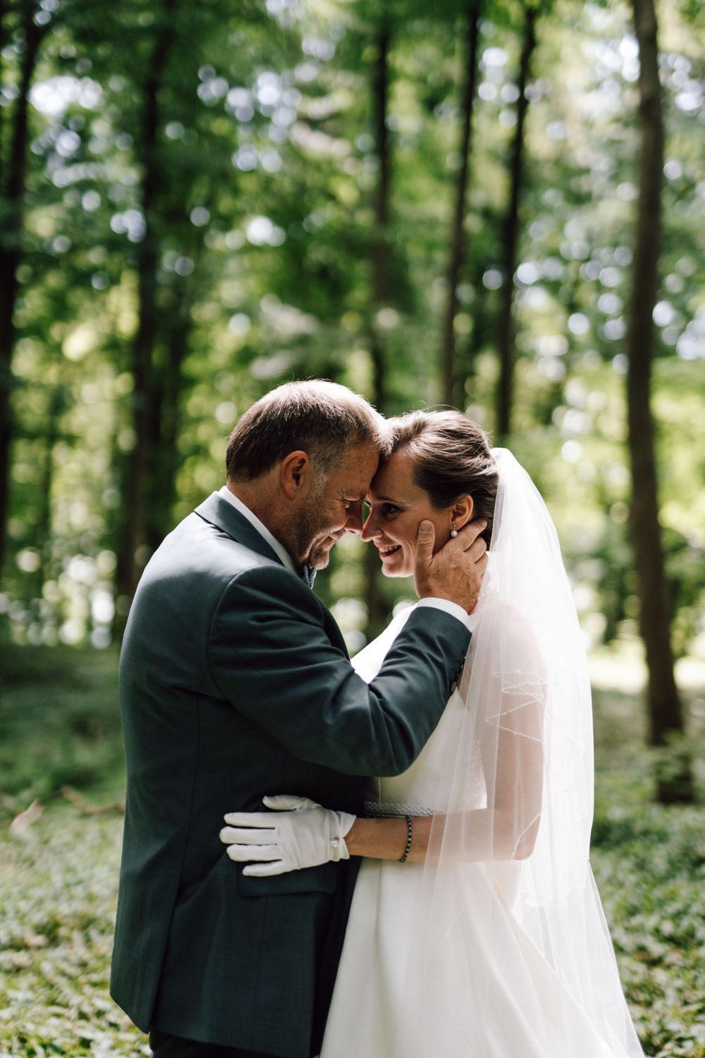Tender embrace between newlyweds in a sunlit forest setting.