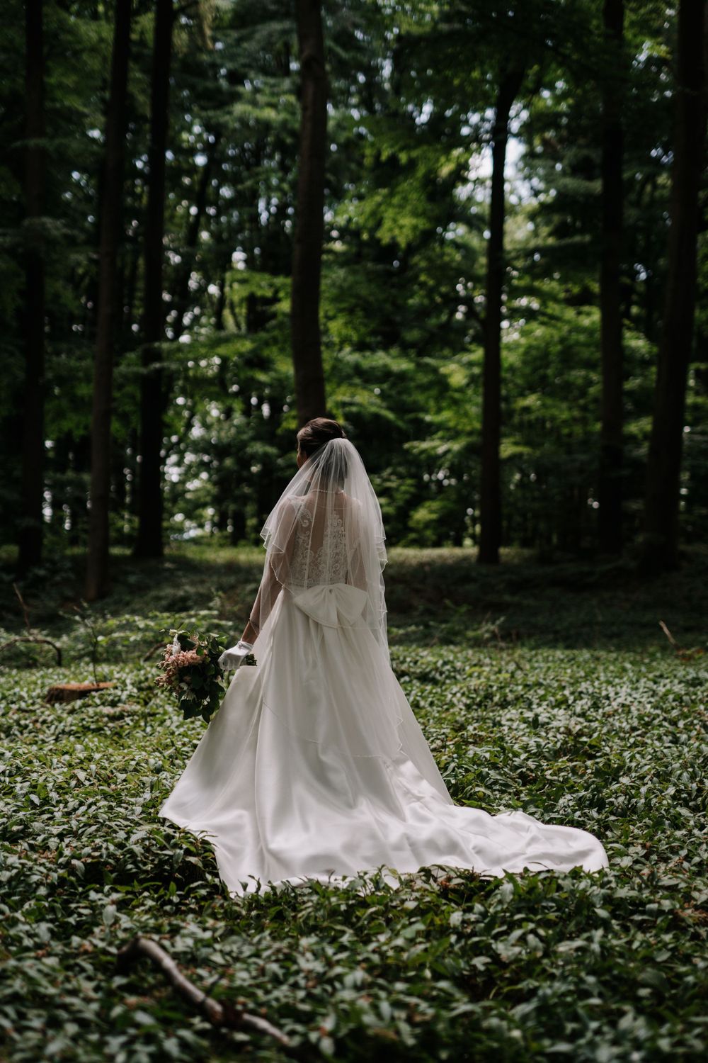 Dramatic wedding dress and veil silhouette against a lush forest backdrop.