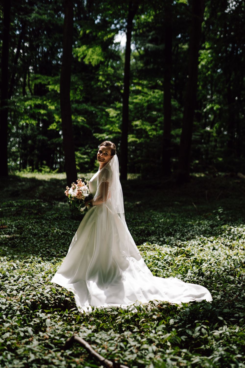 Bride in flowing white gown twirls through a forest clearing filled with wildflowers.
