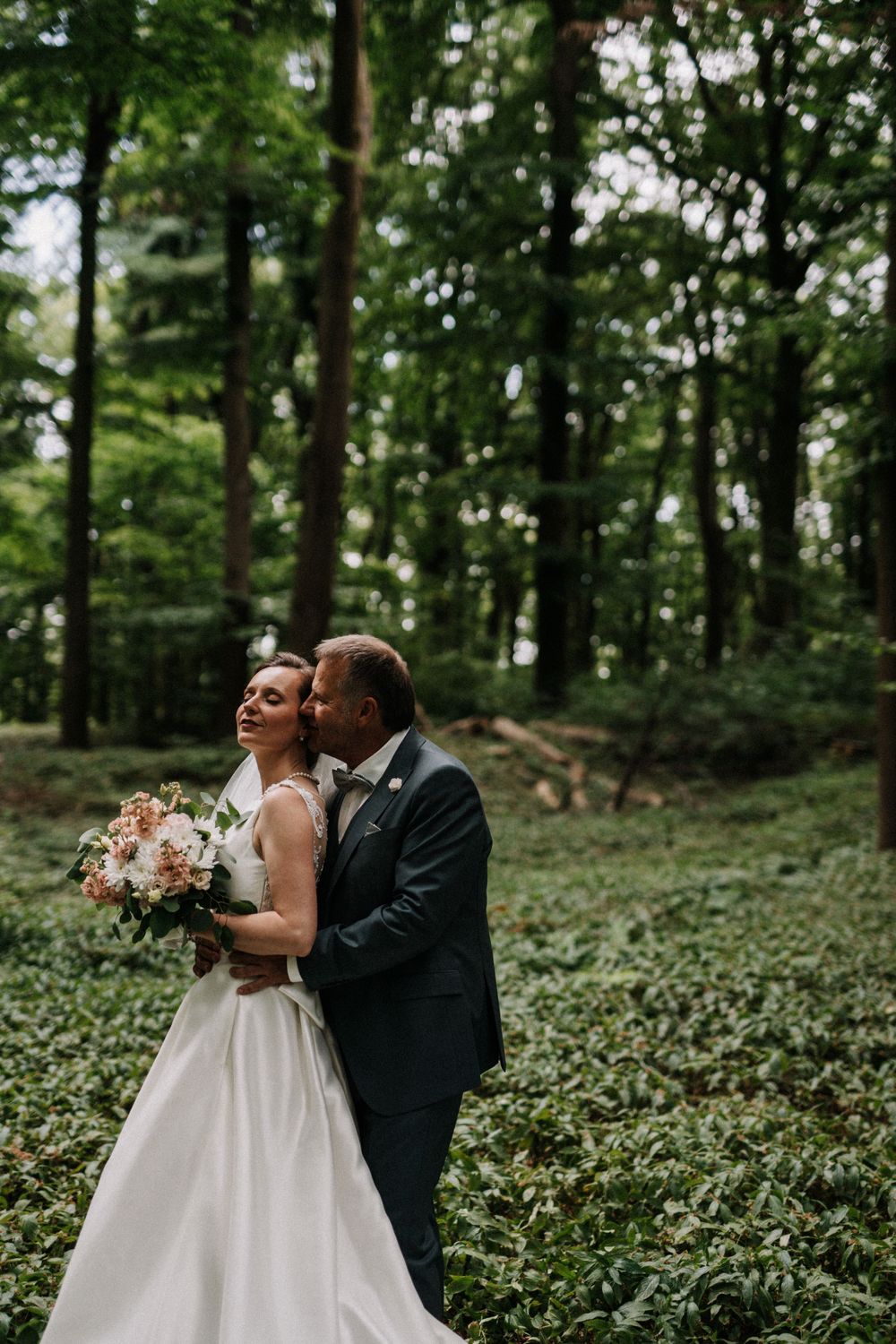 A romantic wedding moment captured in a wooded setting with soft natural lighting.
