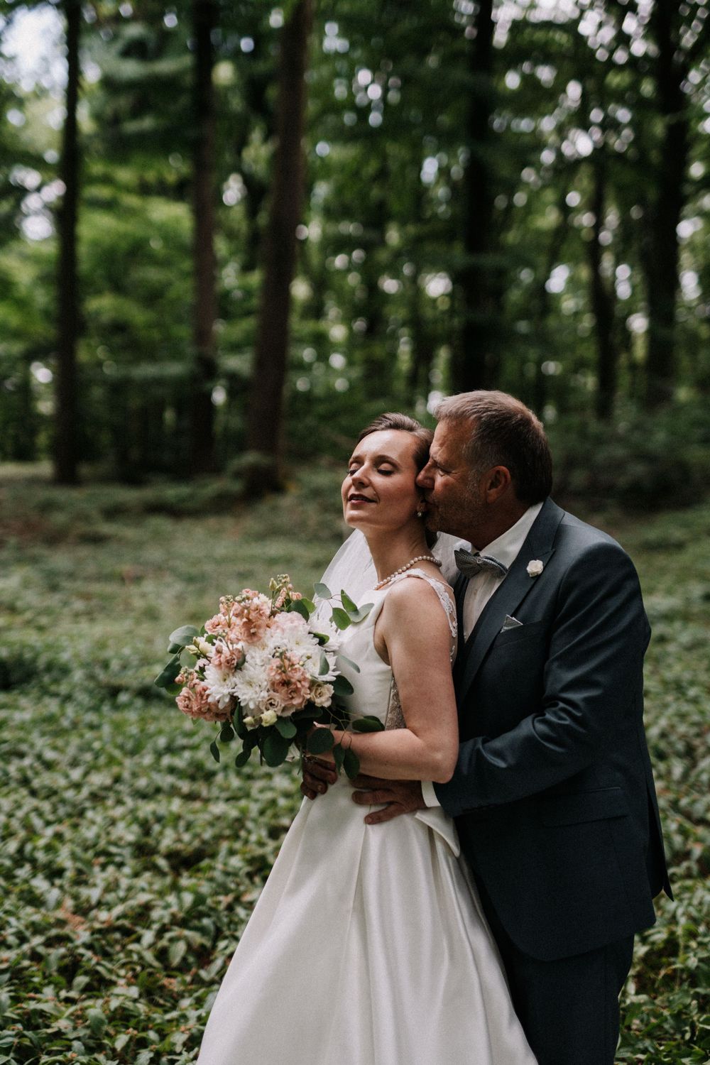 An intimate wedding photo session in a serene forest with sunlight filtering through the trees.