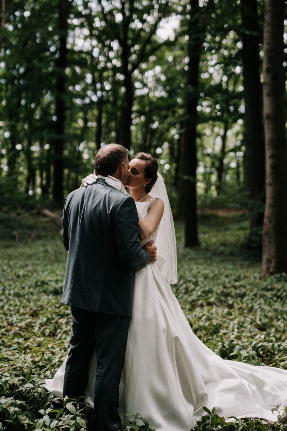 A tender wedding moment photographed against a backdrop of tall forest trees.