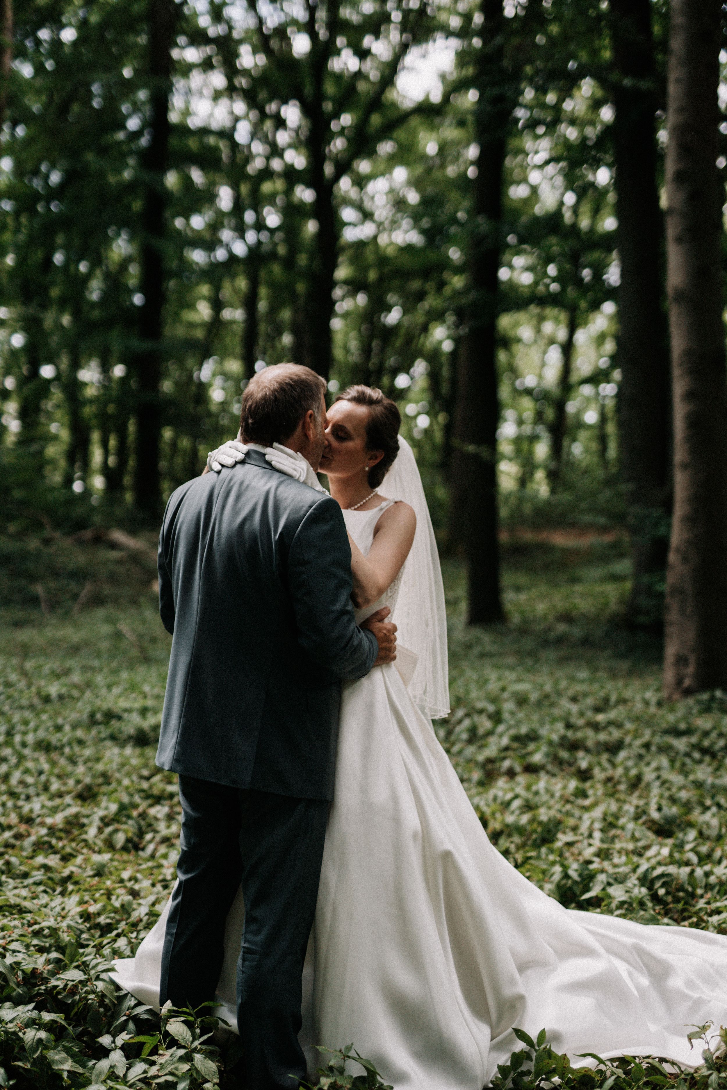 A tender wedding moment photographed against a backdrop of tall forest trees.