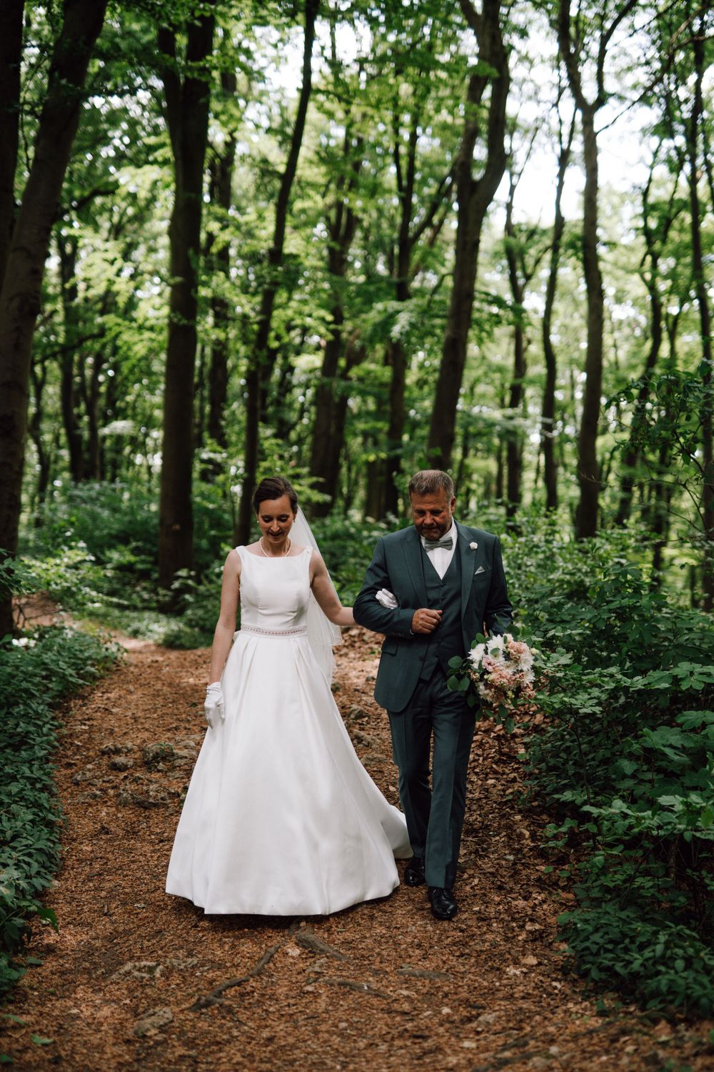 A couple walks hand in hand along a forest path during their wedding photoshoot.