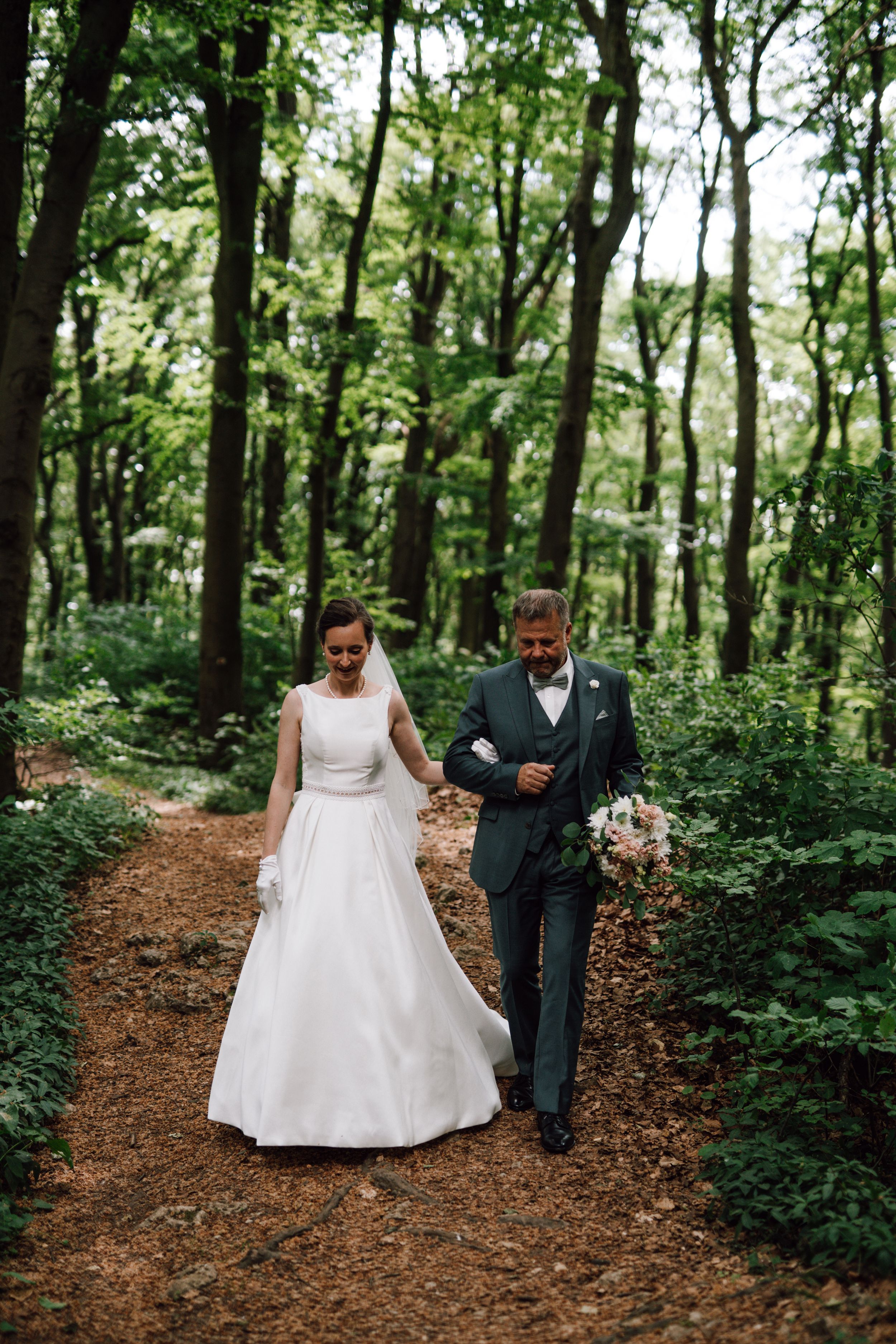 A couple walks hand in hand along a forest path during their wedding photoshoot.