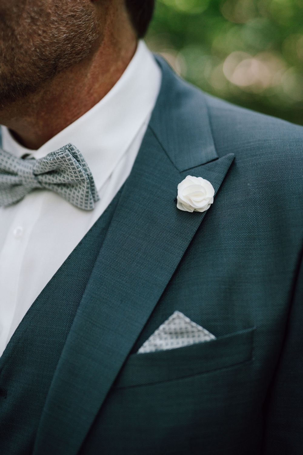 Close-up detail of a dark suit with polka dot bowtie and white boutonniere.