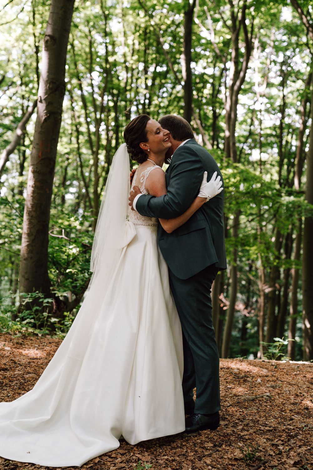 Newlyweds embrace lovingly in a wooded forest setting.