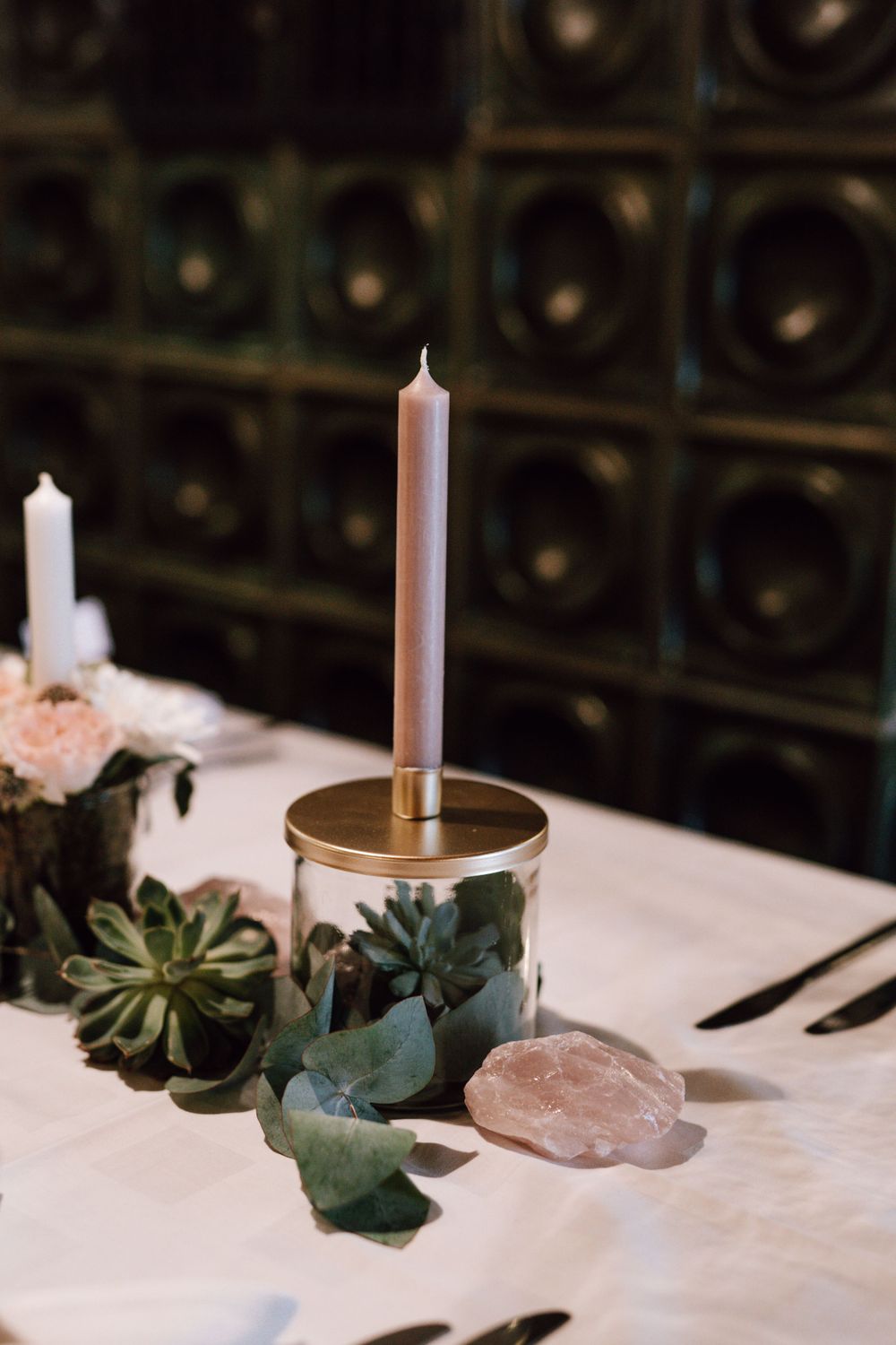 Table setting with tall candle, succulents and crystals against dark background.