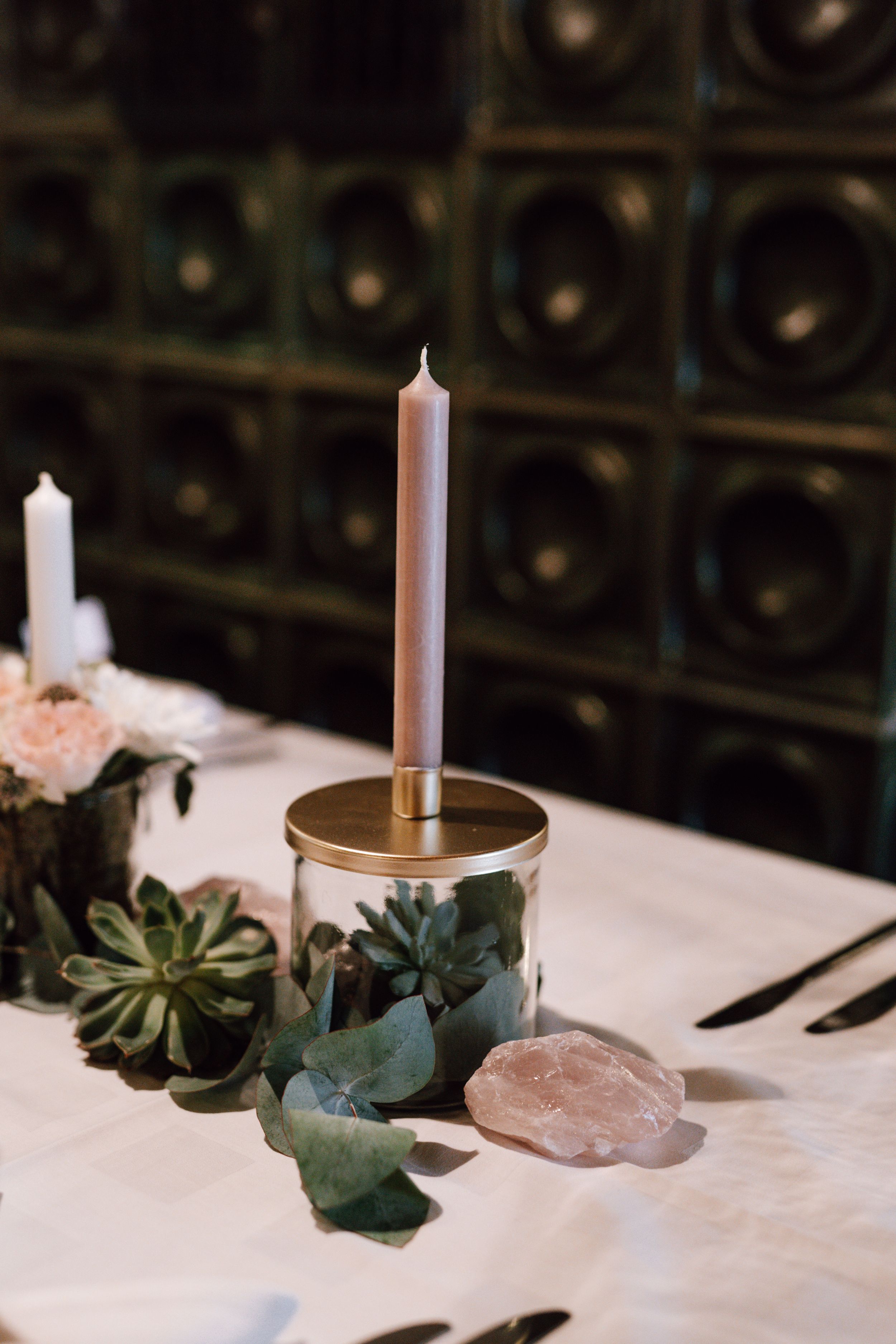 Table setting with tall candle, succulents and crystals against dark background.