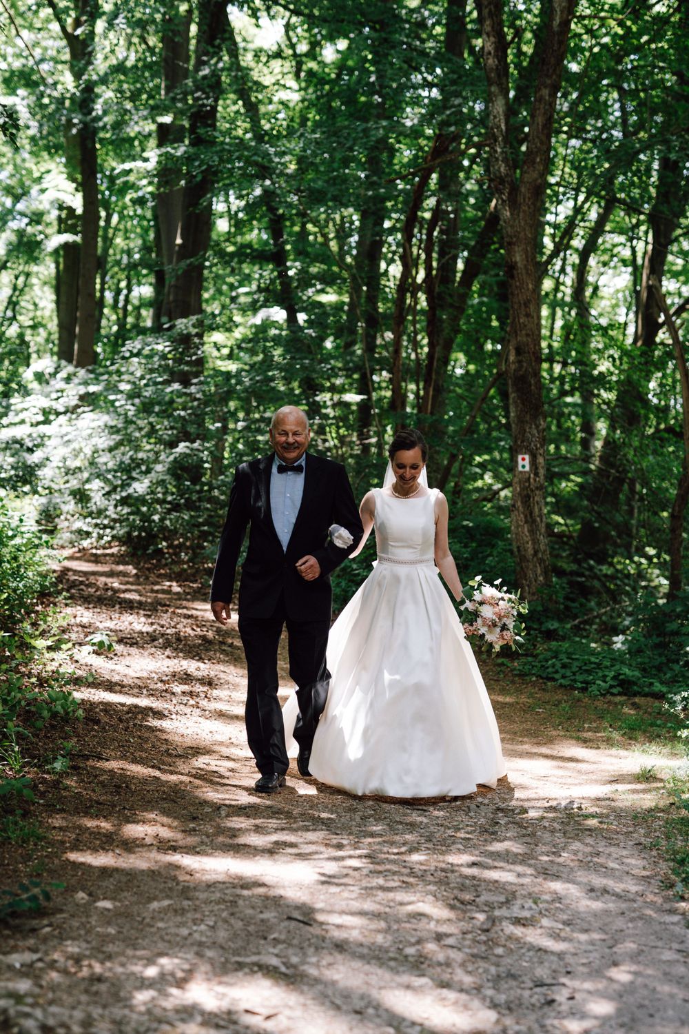 A couple walking down a sunlit forest path during a wedding photoshoot.