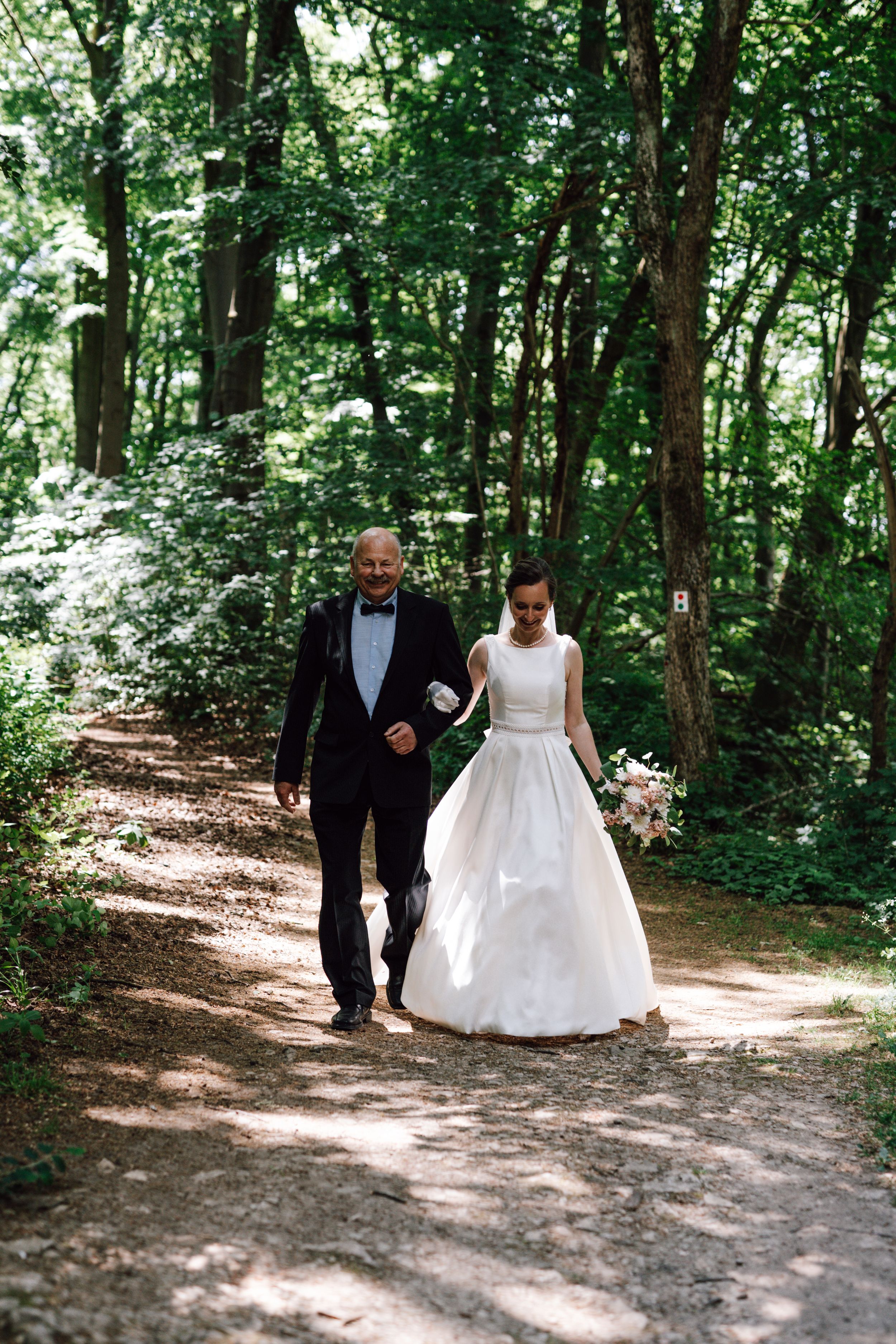 A couple walking down a sunlit forest path during a wedding photoshoot.