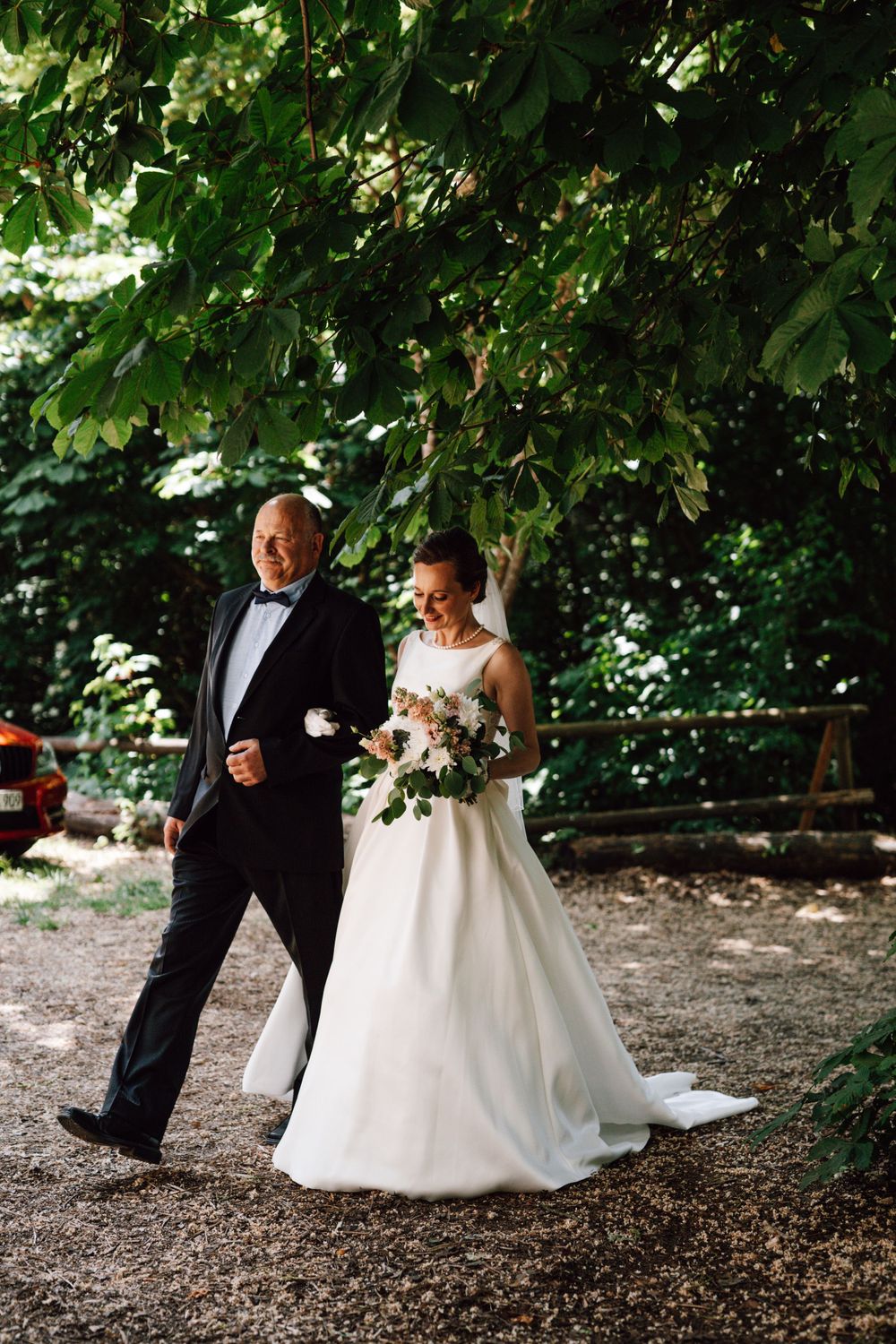 A couple strolling through a wooded area in formal wedding attire.