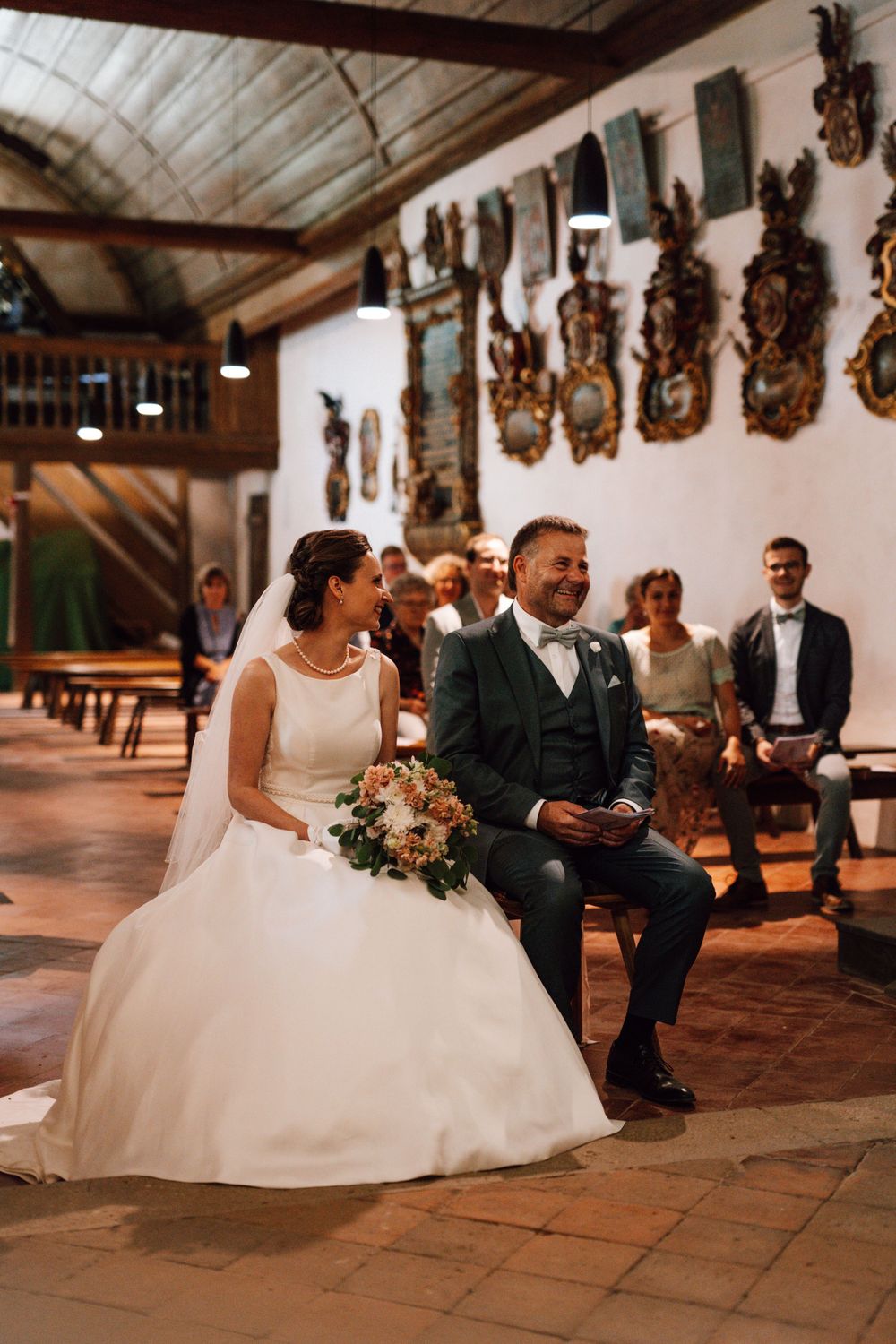 Wedding couple seated in a rustic church with decorative wall ornaments.