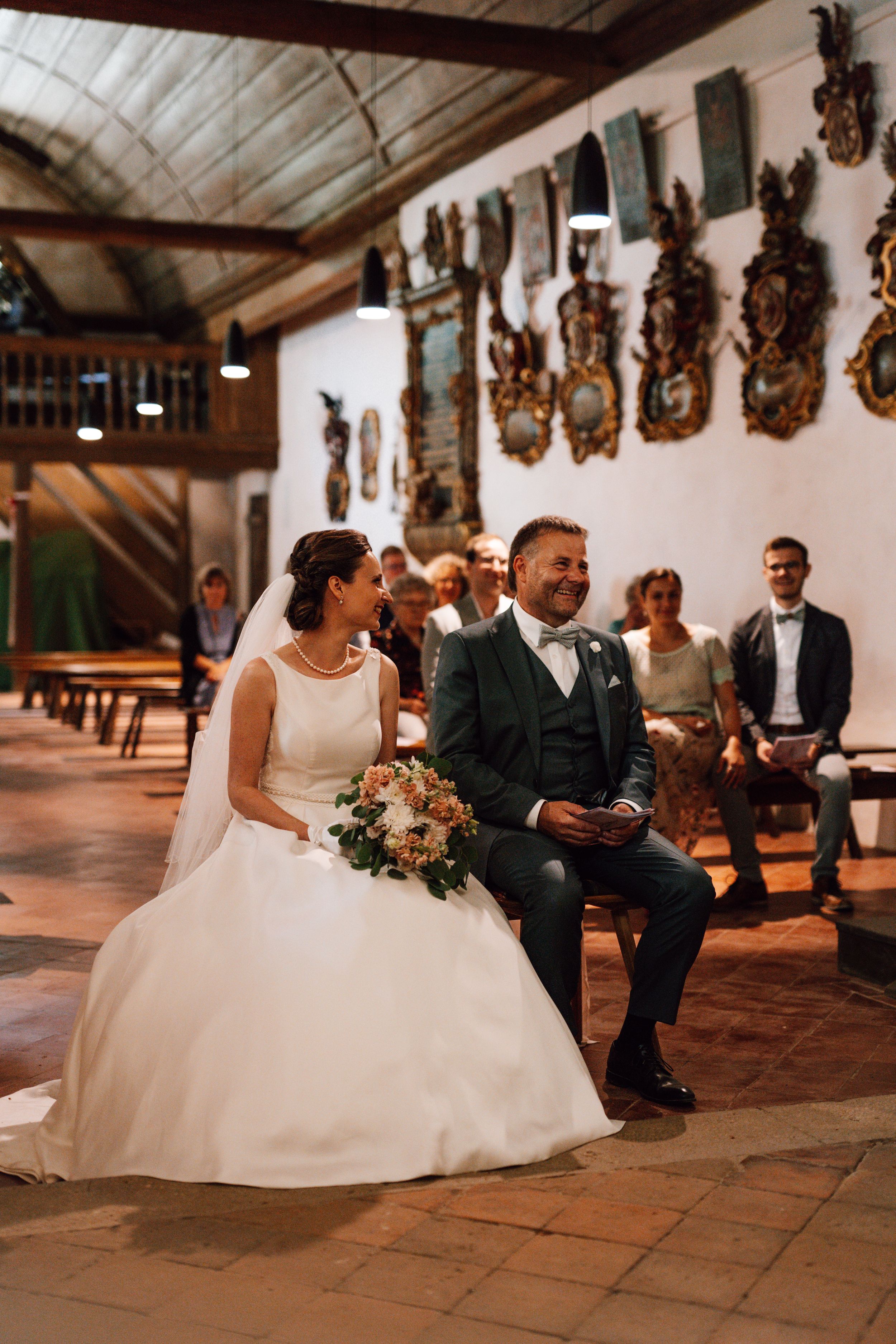 Wedding couple seated in a rustic church with decorative wall ornaments.