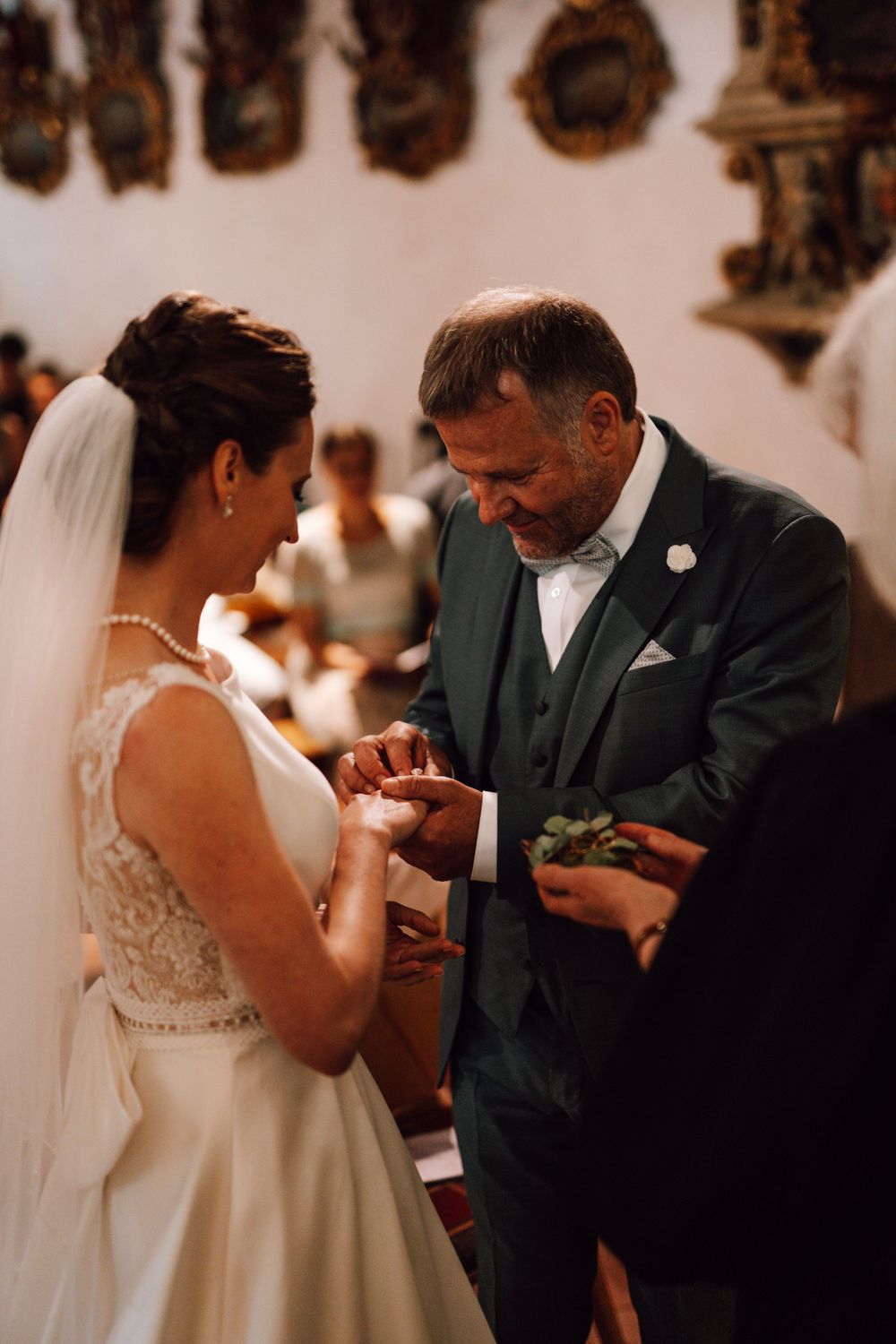 A tender moment during a wedding ceremony as rings are exchanged between the bride in a lace dress and groom in dark suit.
