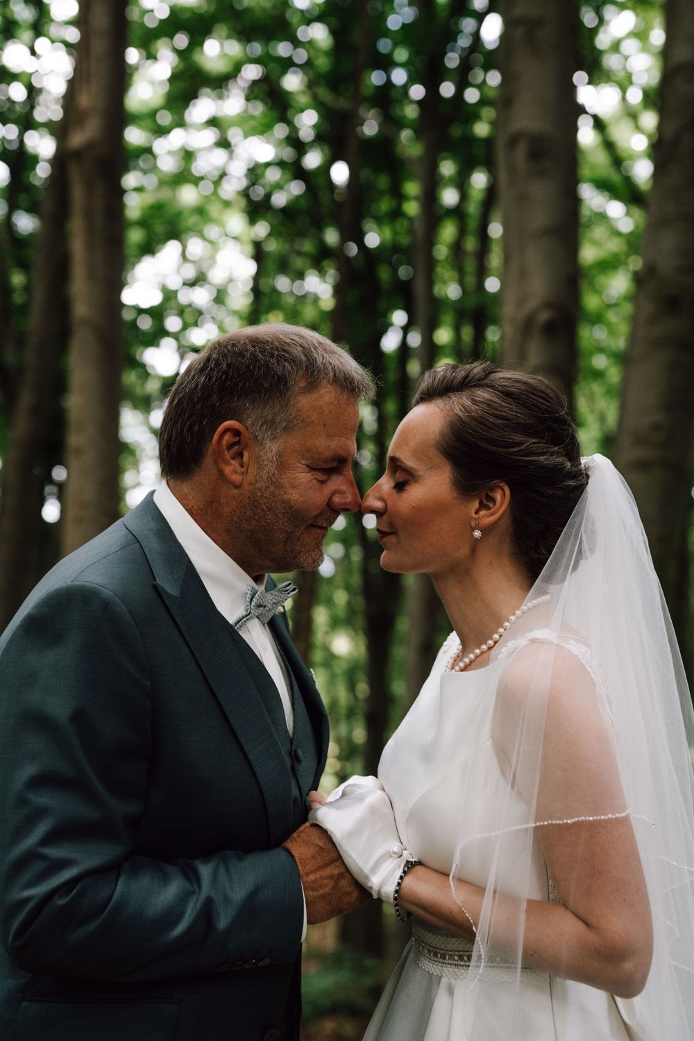 Romantic wedding portrait of couple in woodland setting sharing tender moment under forest canopy.