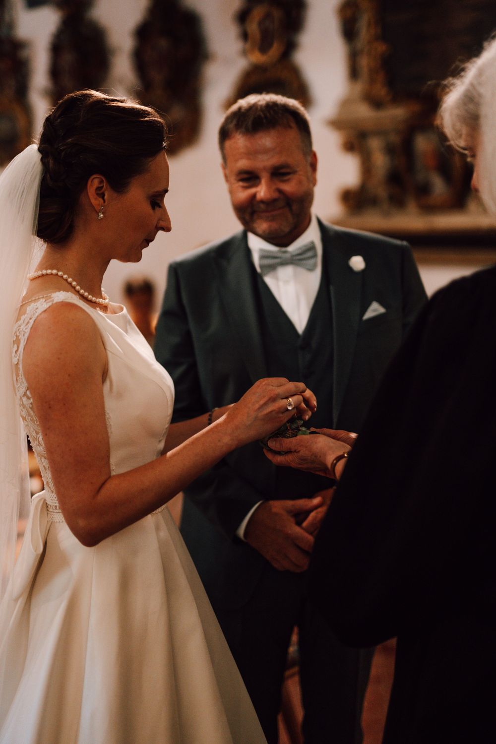 A joyful wedding ring exchange moment captured in a church setting with ornate decorations.