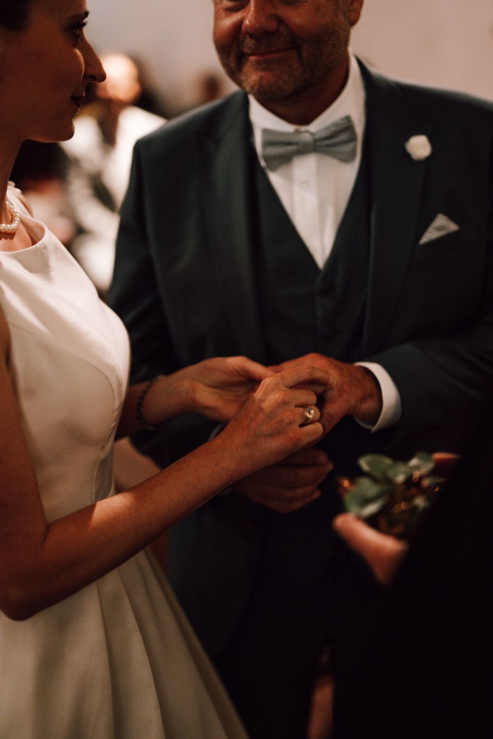 Close-up detail of wedding ring exchange between couple in traditional wedding attire.