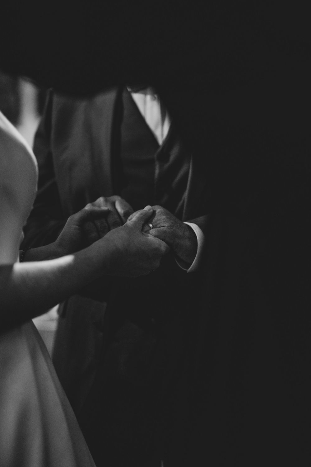 Black and white artistic photo capturing hands during a wedding ring exchange ceremony.
