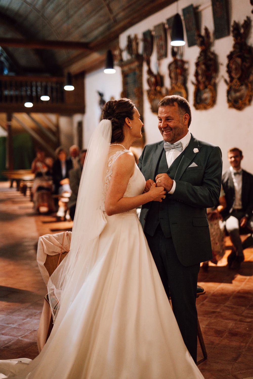 Wedding couple shares a romantic moment in rustic venue with decorative wall art.