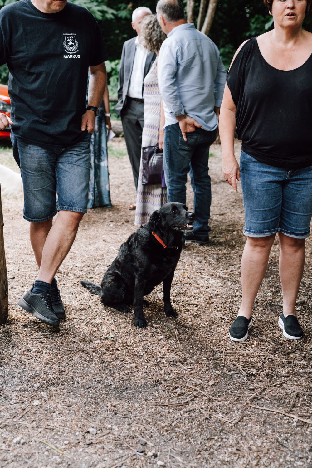 A crowd of people standing on a gravel path wearing casual summer attire.
