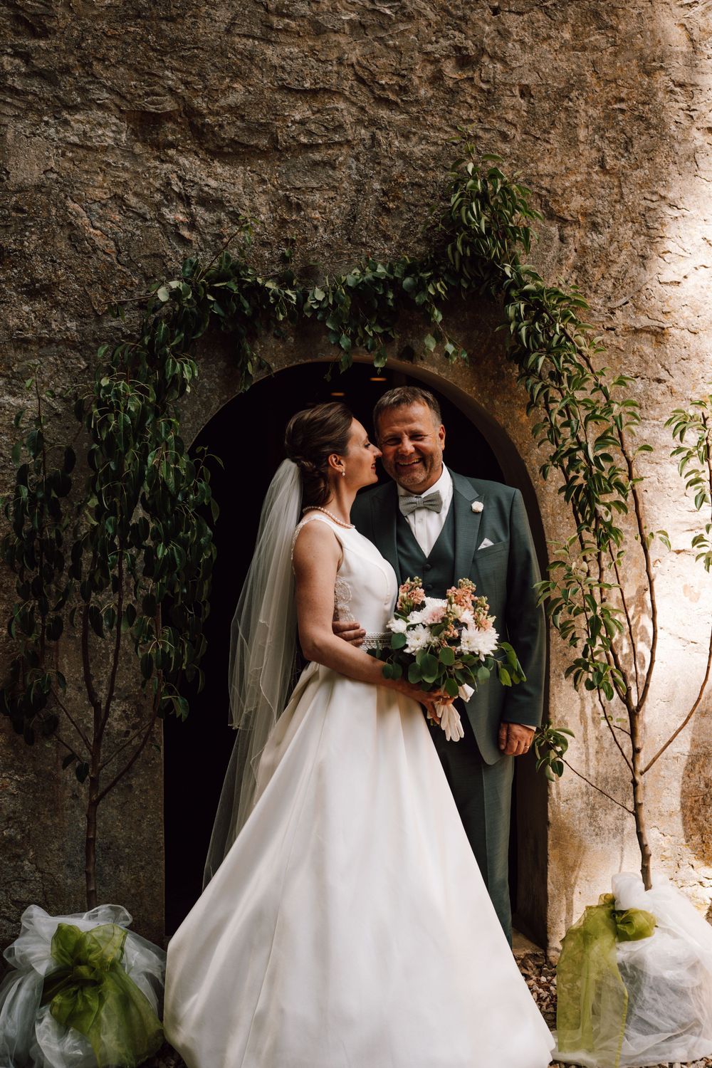 A romantic stone archway decorated with greenery creates an intimate wedding setting.