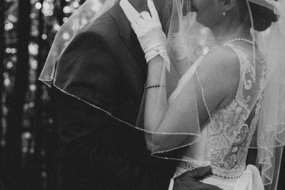 Black and white wedding photo capturing intimate moment between couple under bridal veil.