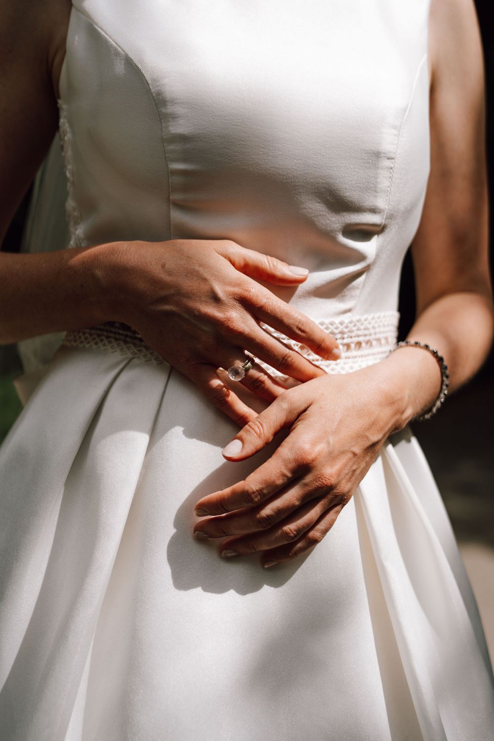 Close-up detail of hands wearing wedding rings against a white dress.