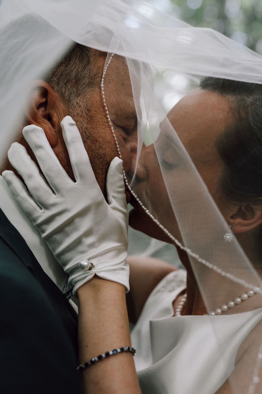 Close-up wedding photo showing intimate moment with bride's gloved hand on groom's cheek under veil.