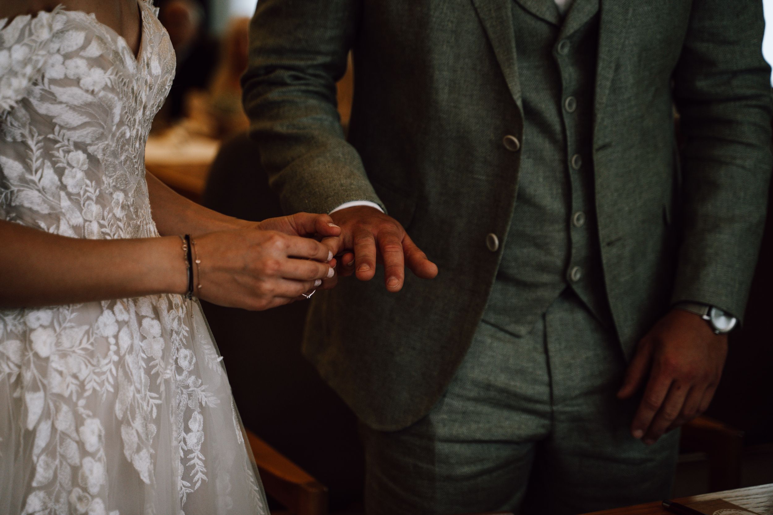 Close-up shot of ring exchange during wedding ceremony with sage green suit detail.