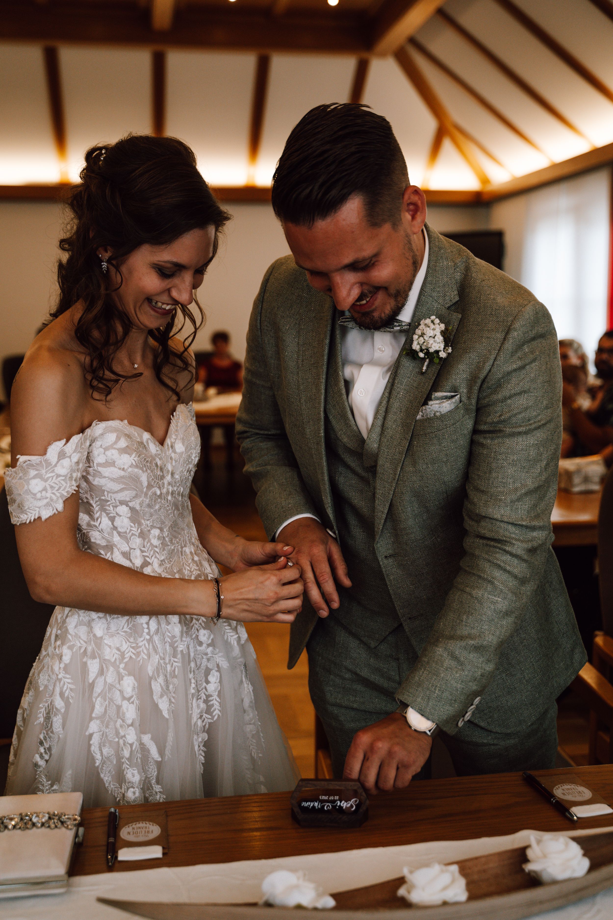 Joyful moment during ring exchange at wedding ceremony with wooden ceiling detail.