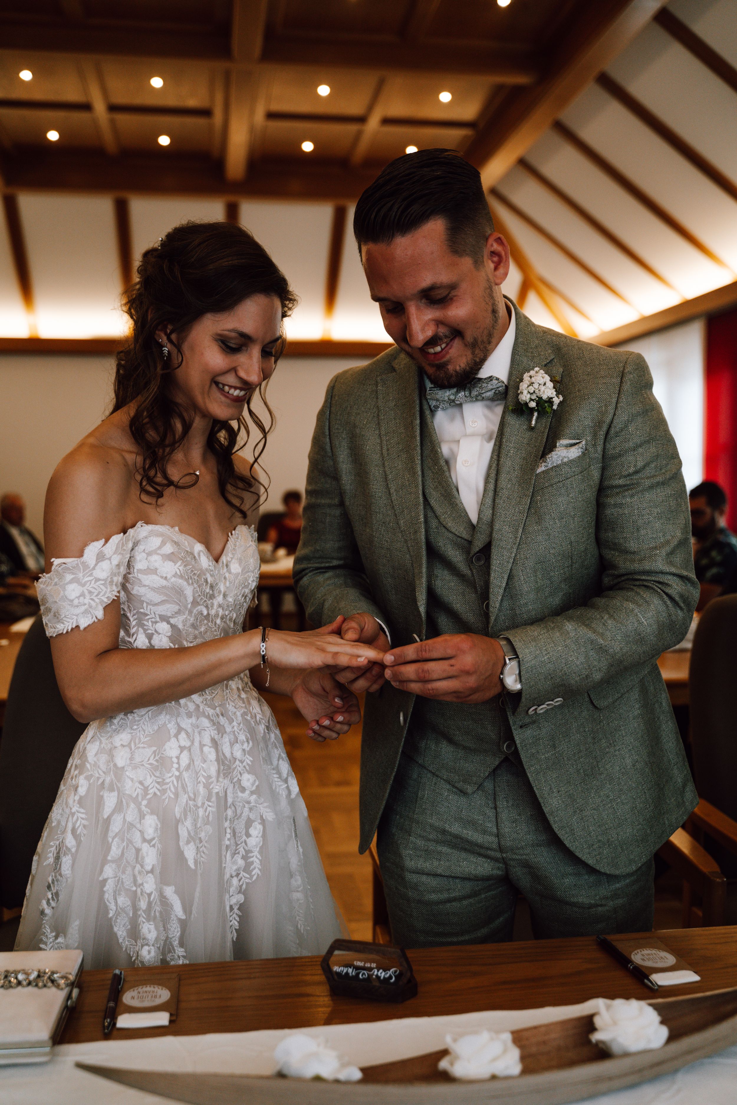 Happy exchange of rings during wedding ceremony in room with wooden architectural details.