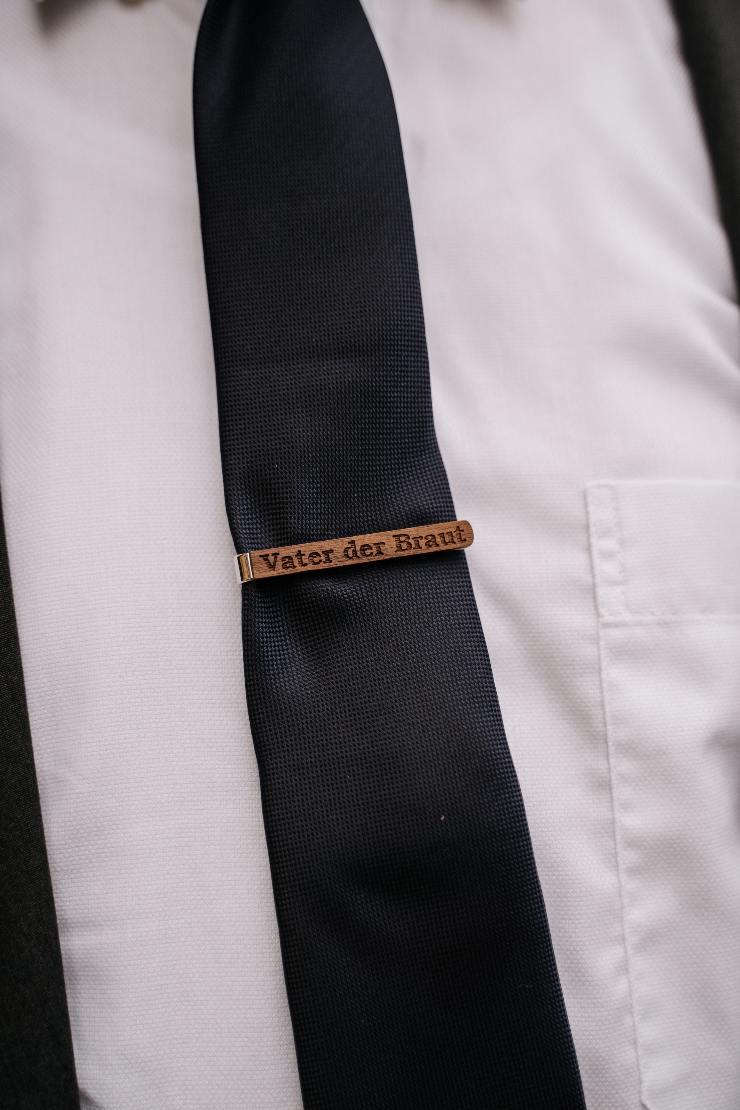 Wooden tie clip with engraved text on a black and white formal attire.