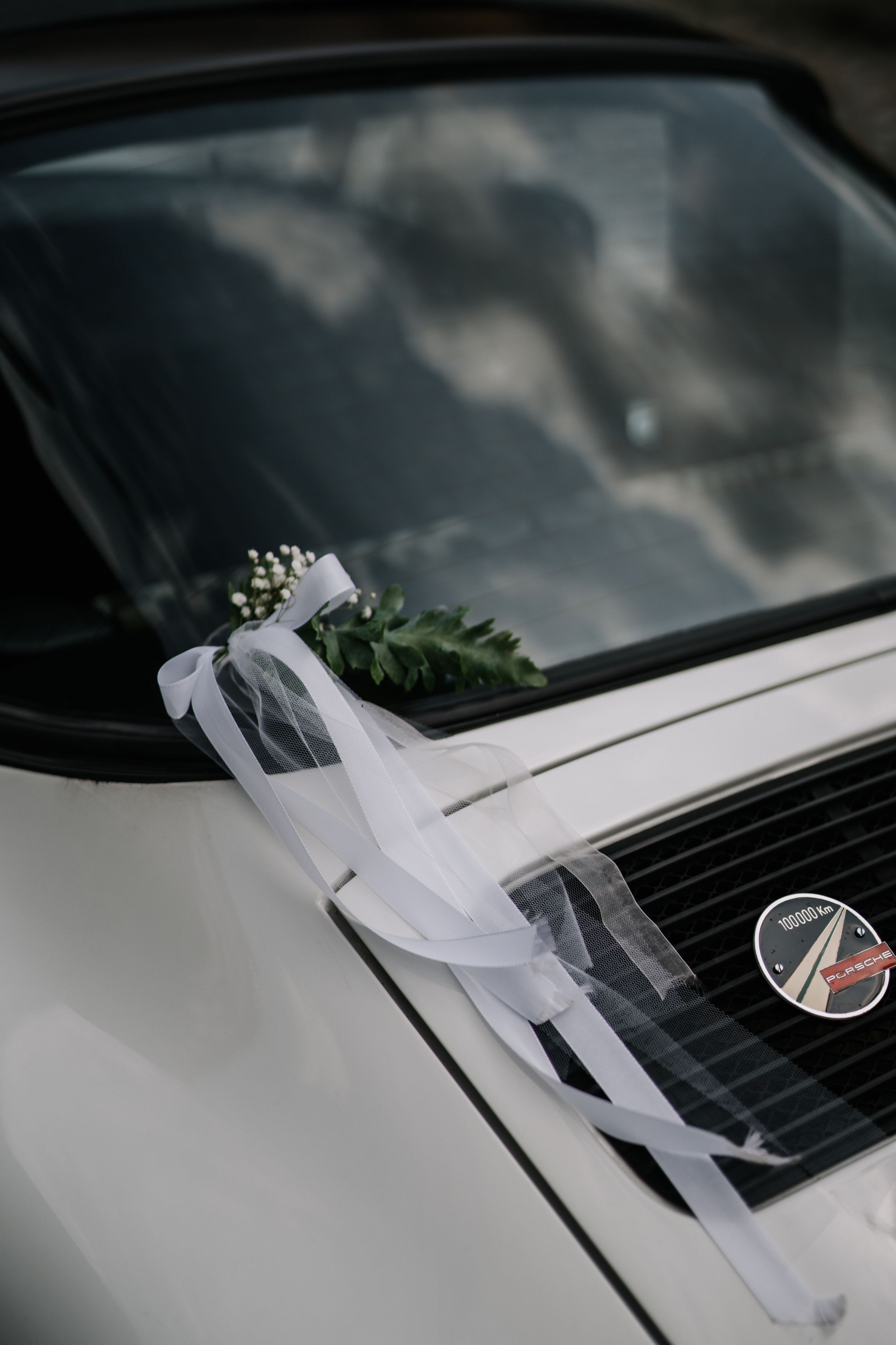 White ribbons and wedding decorations adorn the hood of a modern car.