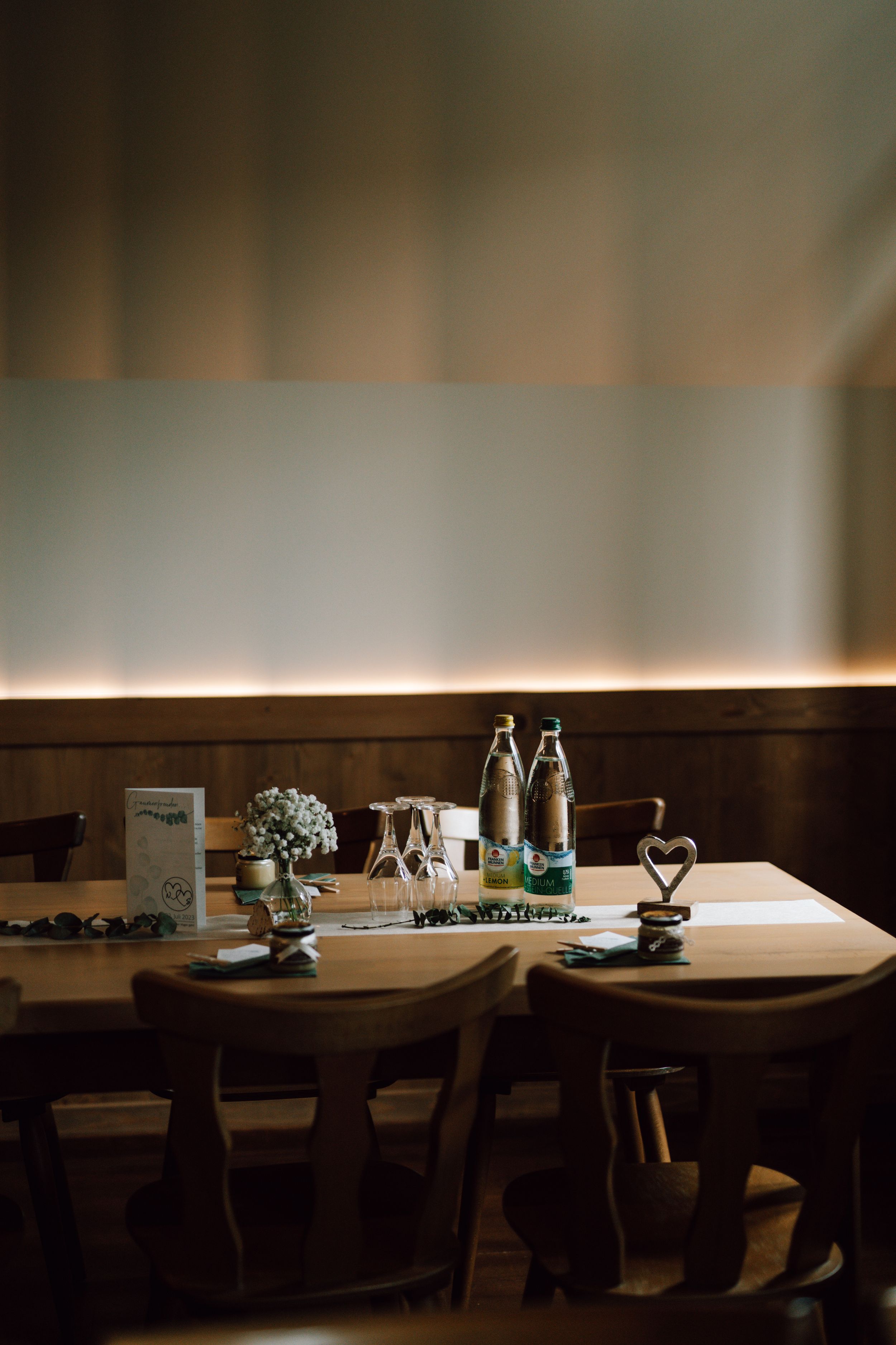 Romantic restaurant table setting with glass bottles and heart decor in moody lighting.
