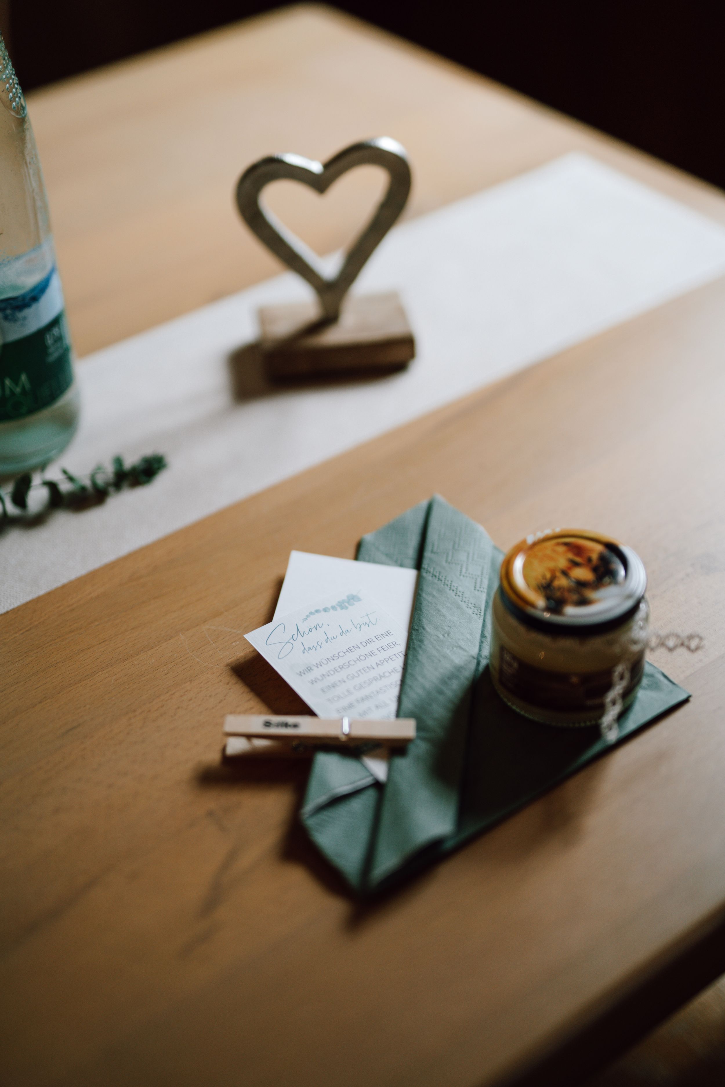 Close-up of table decor with heart stand, napkin, and jar on wooden surface.
