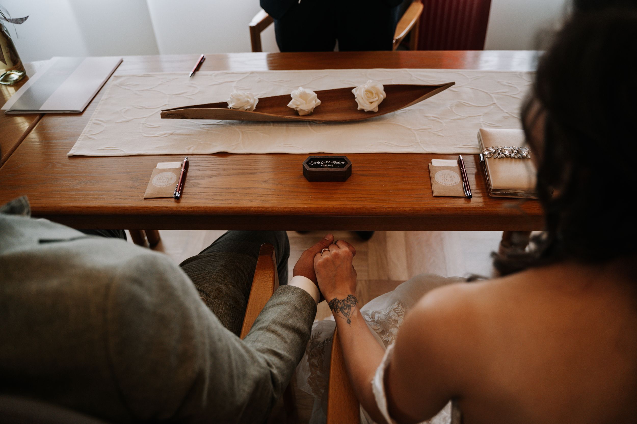 Close-up view of hands and paperwork on a wooden table during a wedding ceremony.