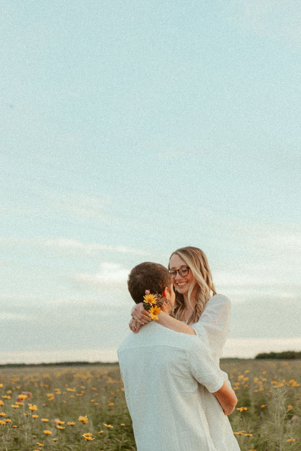 Couple embracing in sunlit field of yellow wildflowers during sunset.