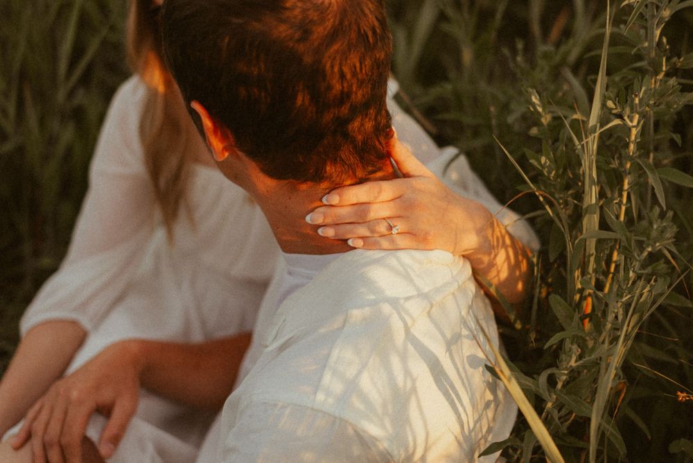 Close-up of hands embracing in warm sunlight among tall grass.