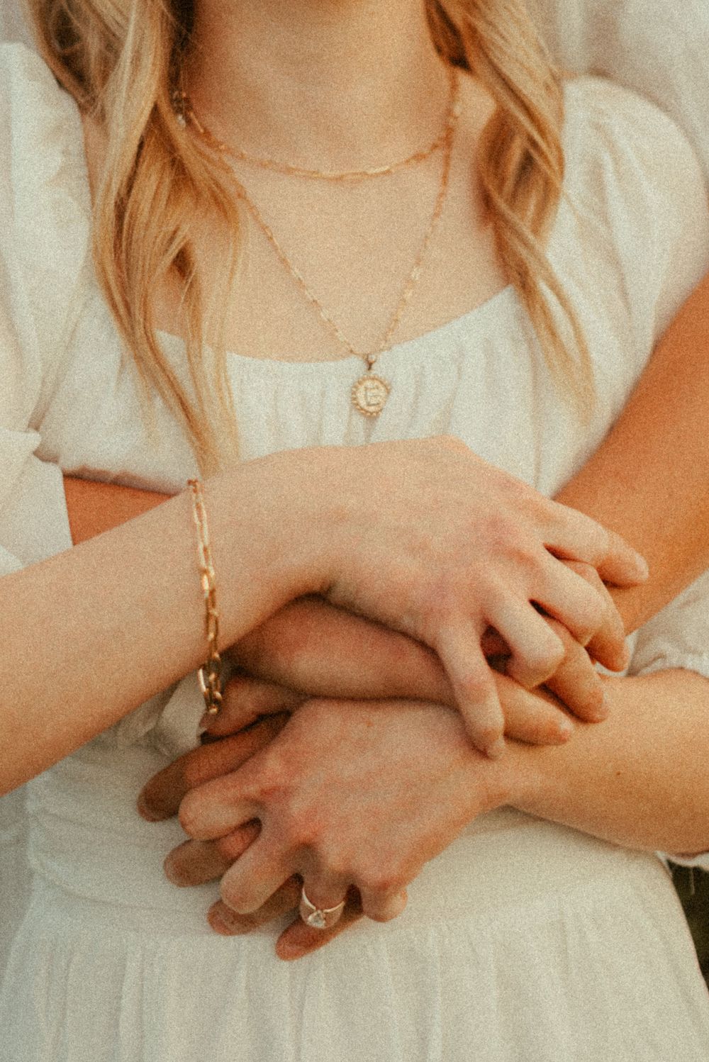 Close-up of intertwined hands with delicate jewelry and white dress details.