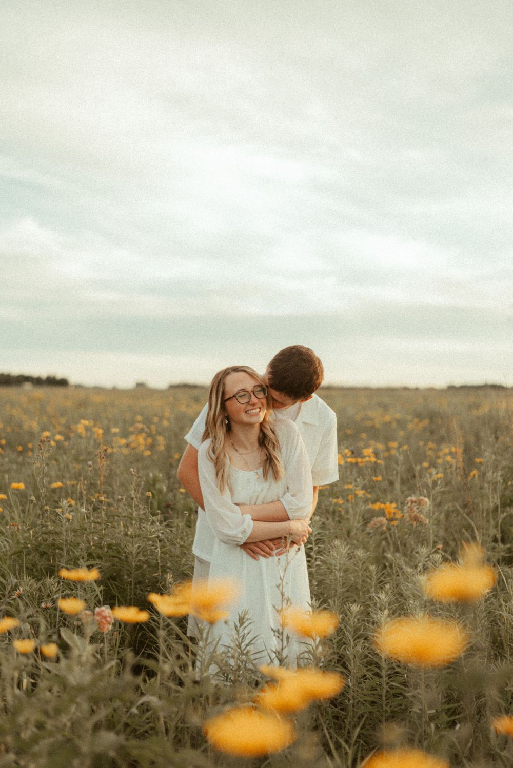 Romantic embrace in a sunlit meadow filled with yellow wildflowers.