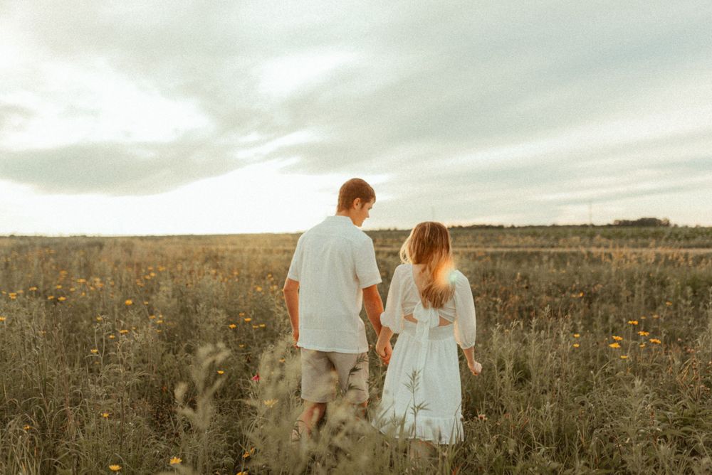 Couple walking through a golden wildflower field at sunset.