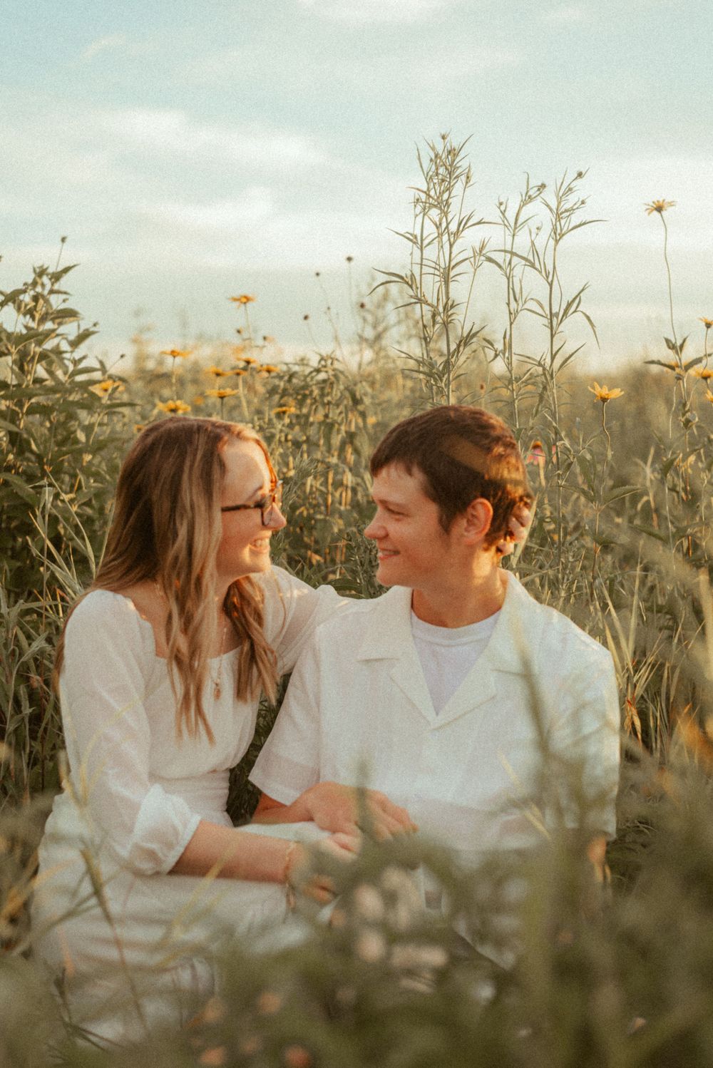 Intimate moment shared between couple in white clothing amid wildflowers at sunset.