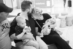 Black and white photo of family members holding infants in a casual indoor setting.
